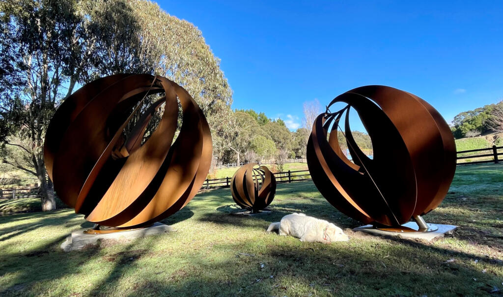 Large Sphere Sculptures made from rusted Corten Steel in a rural garden setting;