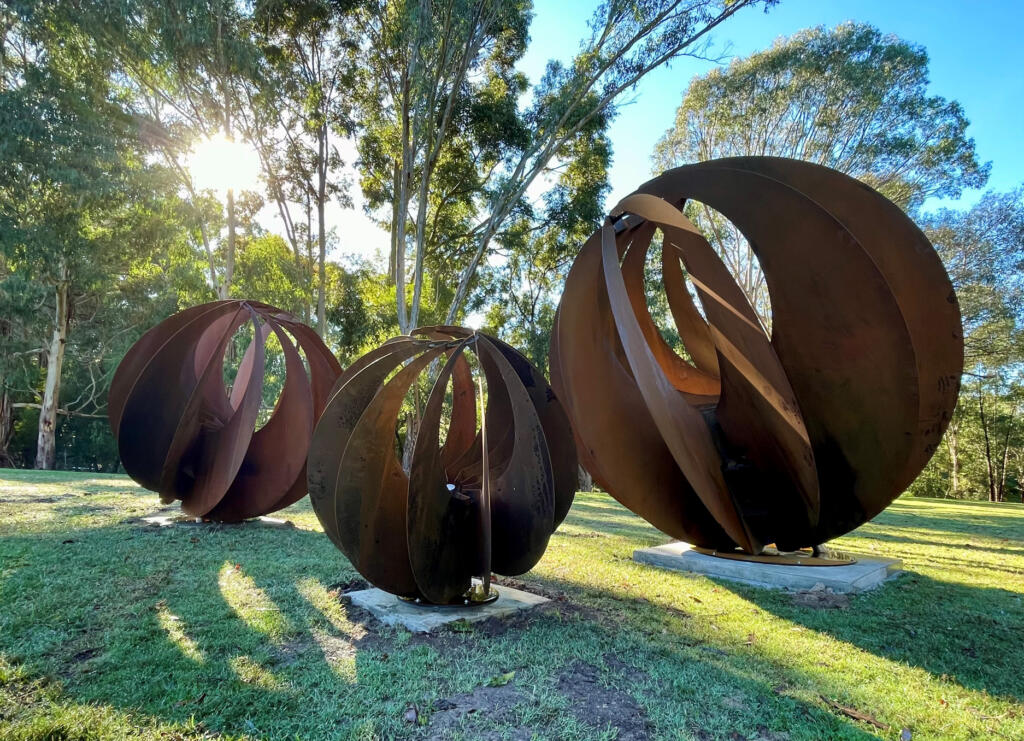 Large Sphere Sculptures made from rusted Corten Steel in a rural garden setting;